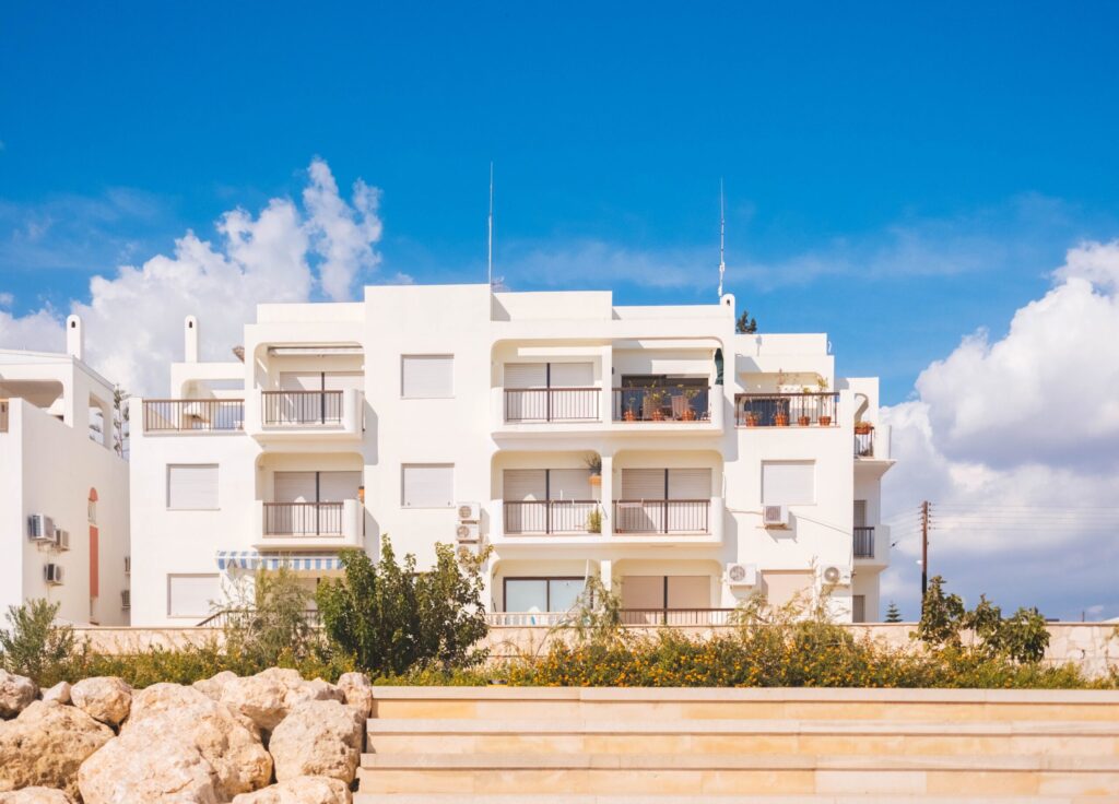 White low-rise apartment building with balconies under a bright blue sky and white clouds