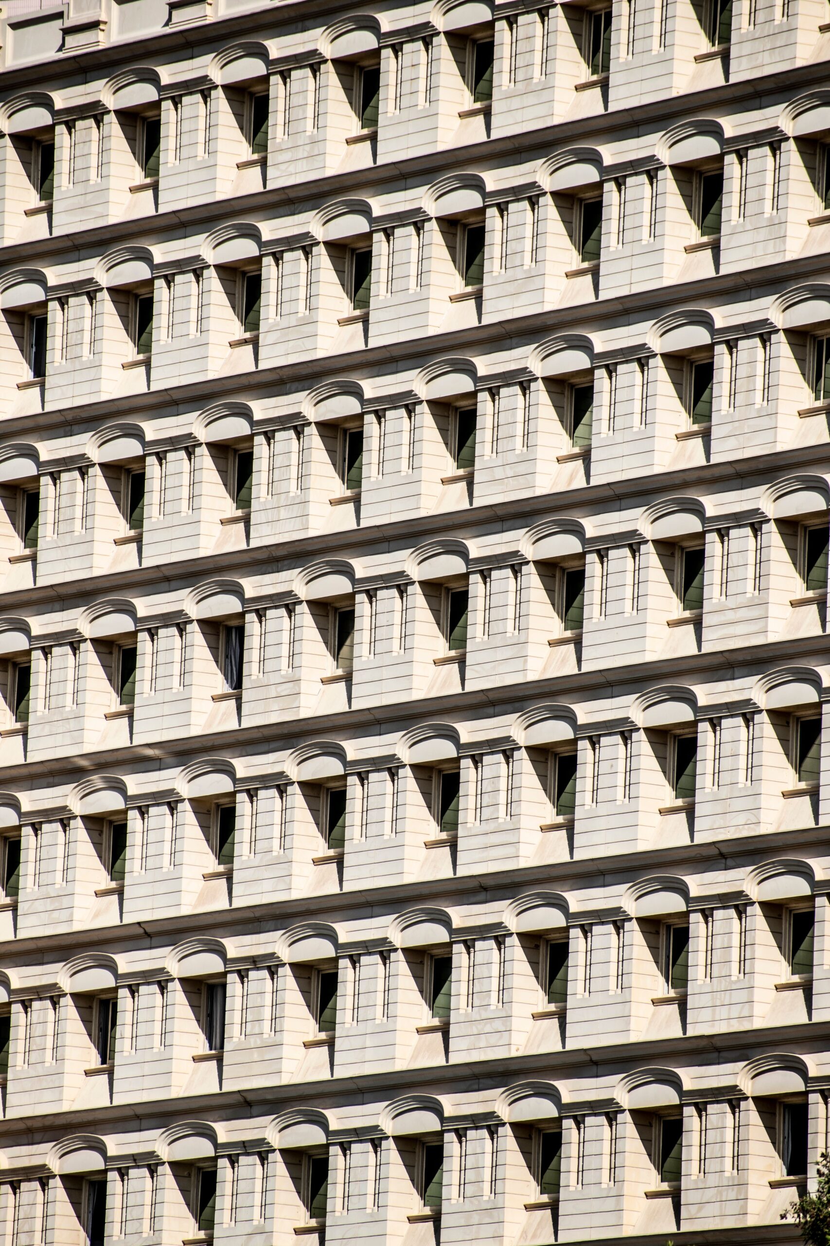 Repeating pattern of cream apartment building window bays with arched balcony canopies against a blue sky in Dubai