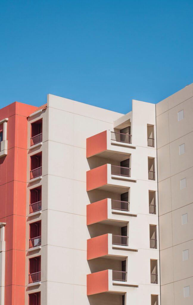 Mid-rise apartment building facade in warm terracotta and cream tones with stepped balconies against a clear blue sky, representative of Canal Residence West Mediterranean Building in Dubai Sports City, Dubai