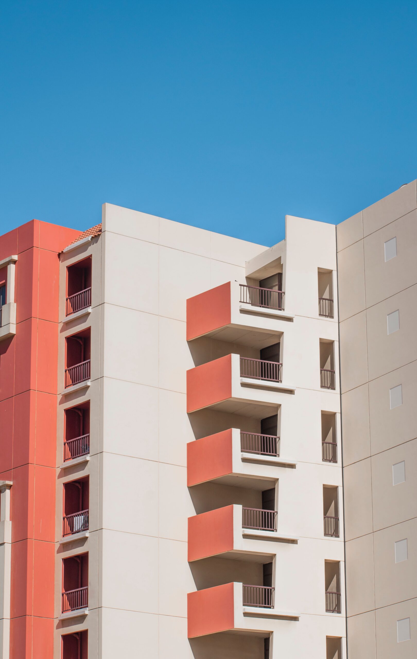 Mid-rise apartment building facade in warm terracotta and cream tones with stepped balconies against a clear blue sky, representative of Canal Residence West Mediterranean Building in Dubai Sports City, Dubai