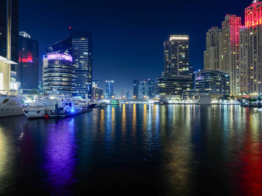 Illuminated Dubai Marina skyline and yachts reflected in the water at night
