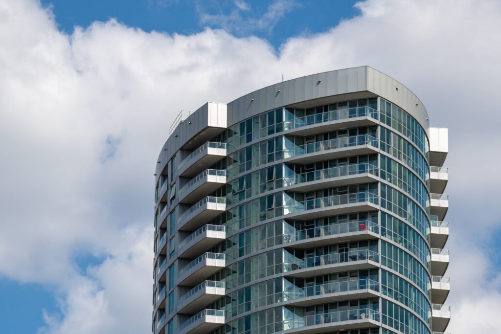 Curved glass residential tower with balconies against a cloudy blue sky