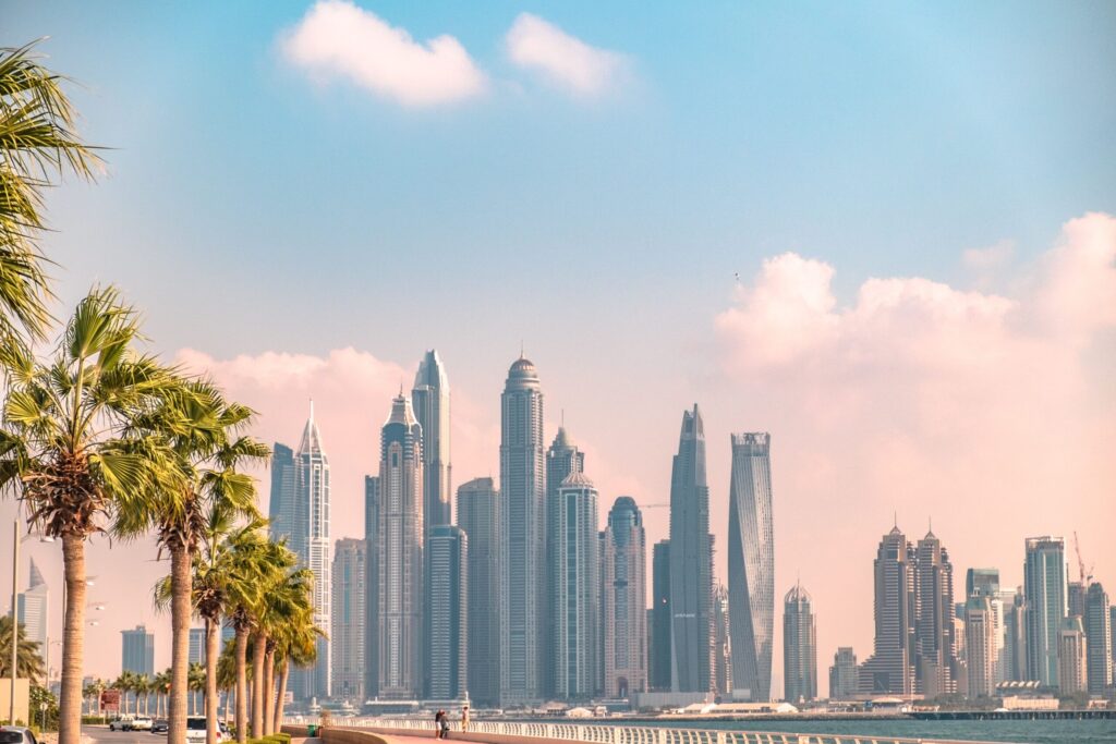 Dubai skyline of modern high-rise towers viewed past palm trees under a clear blue sky, near Sobha Creek Vistas Heights