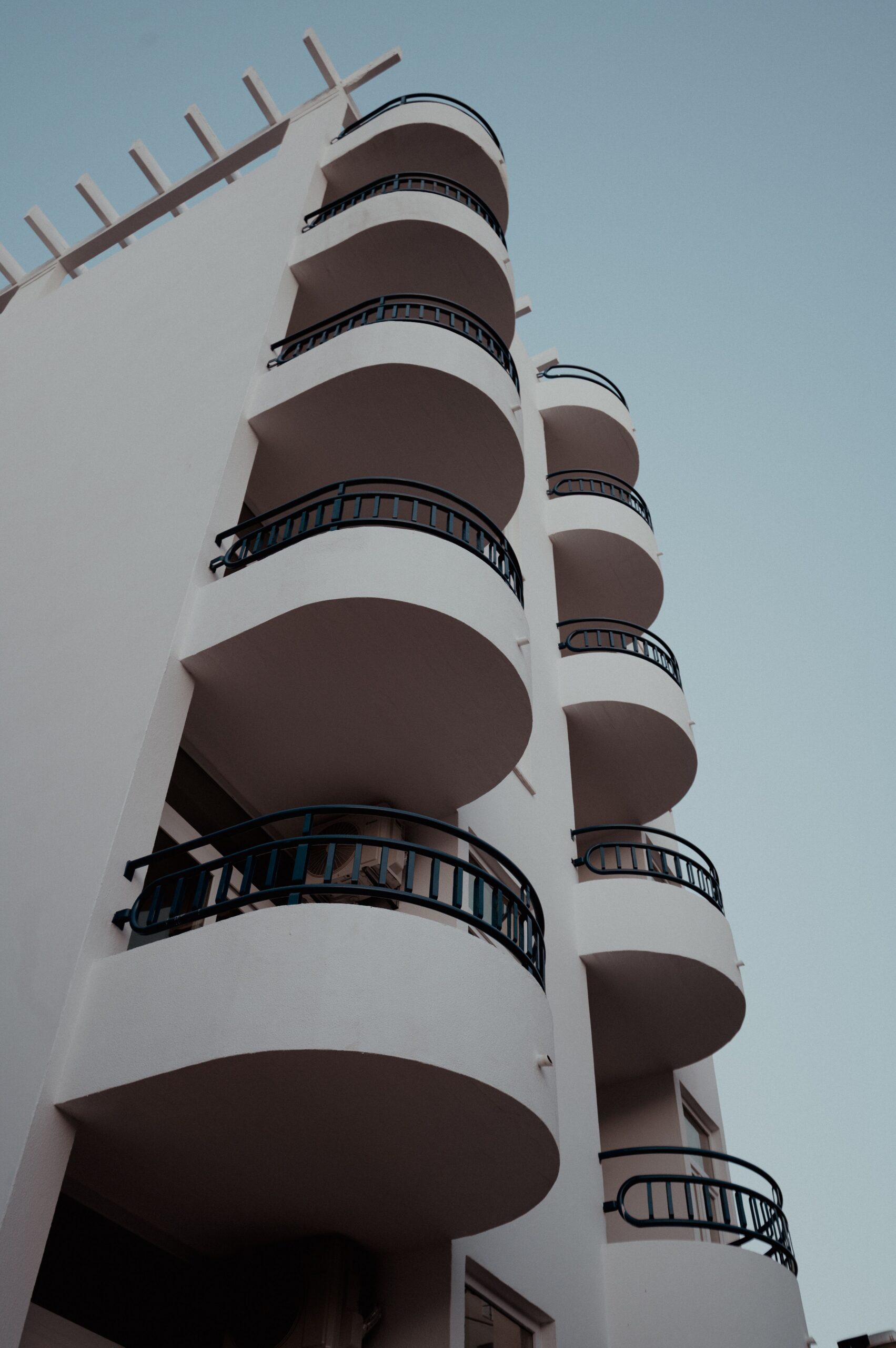 Low-angle view of a cream-toned Dubai mid-rise apartment building with rows of curved balconies against a clear sky, representative of the residential architecture near H3 by Aurora, JVC