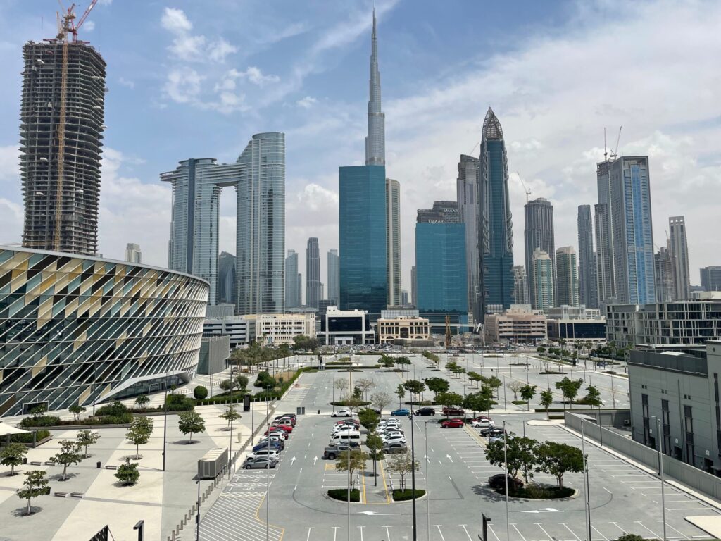 Daytime Downtown Dubai skyline with Burj Khalifa and a tower under construction, seen from a nearby plaza