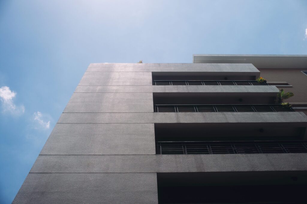 Low-angle view of a modern low-rise residential building facade with balconies against a clear blue sky, similar in scale to Park Lane 2 by Heilbronn's JVC setting