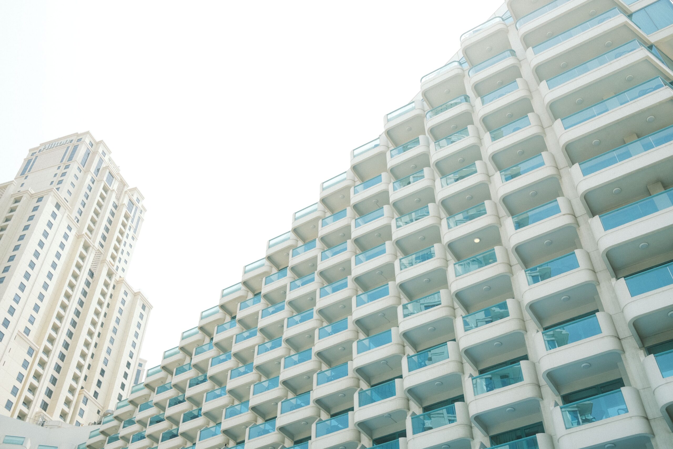 Stepped modern Dubai residential tower with glass balconies against a hazy sky, a second tower visible in the background
