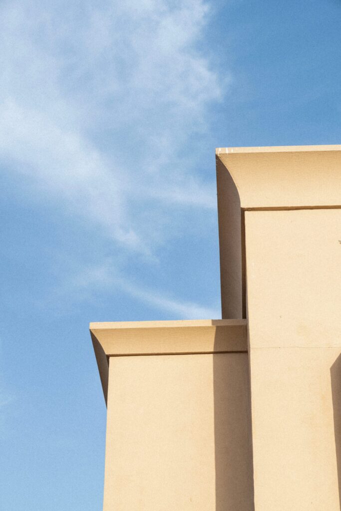 Clean corner of a modern cream-toned building against a soft blue sky with light clouds in Dubai