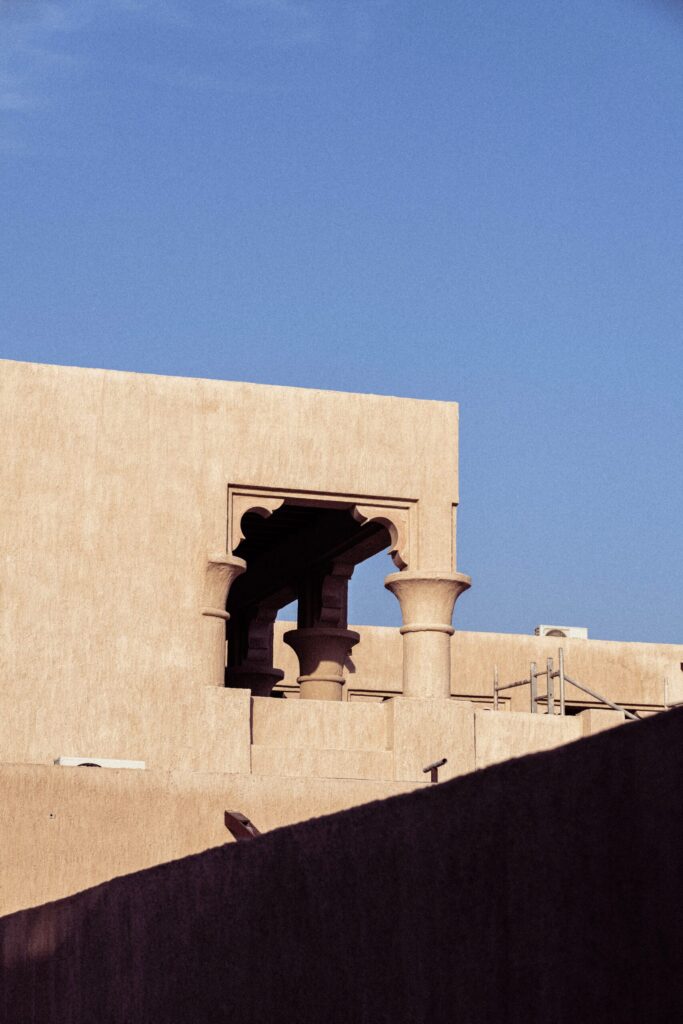 Sandstone Arabian-style building exterior with an ornate carved archway and stone columns under a clear blue sky, no people visible