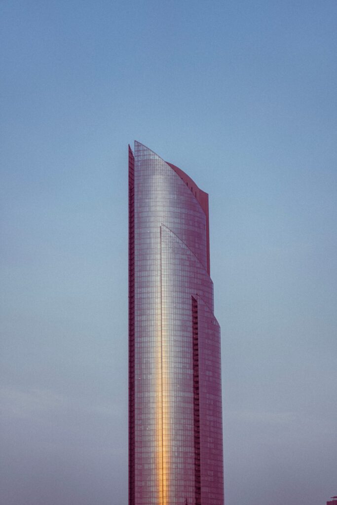 Tall curved glass skyscraper reflecting golden sunset light against a blue sky in Dubai