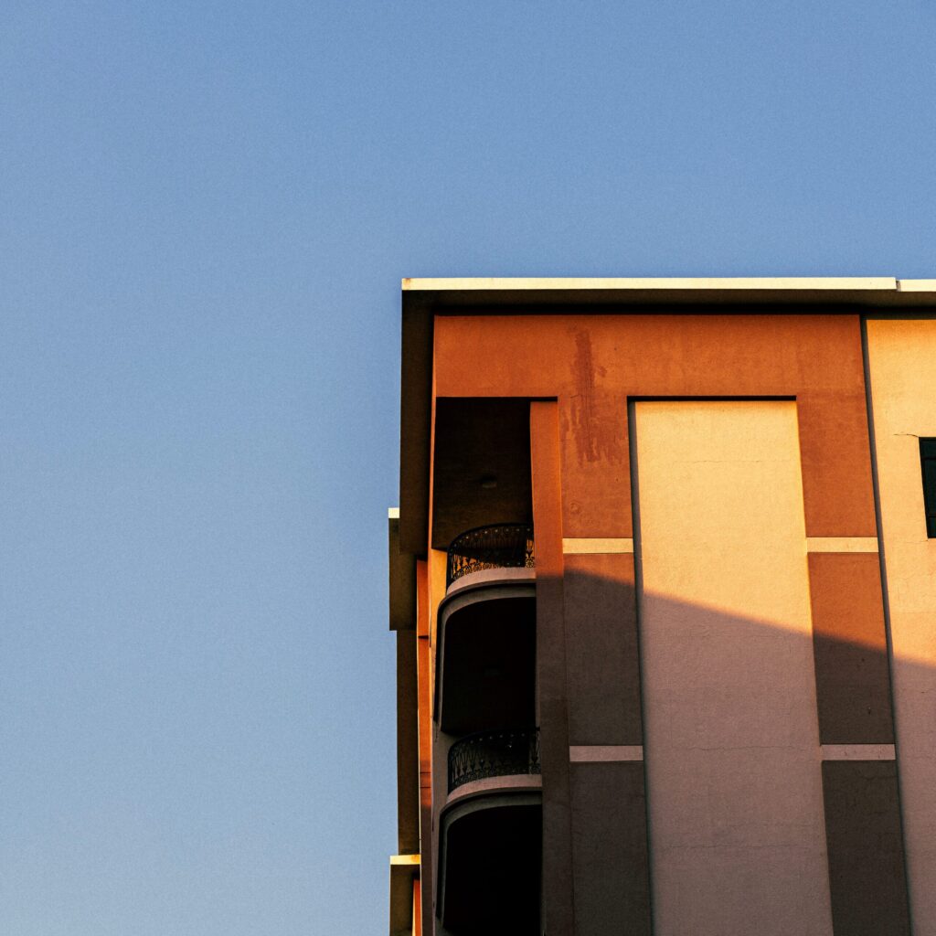 Warm sunset-lit corner of a low-rise apartment building with decorative wrought-iron balcony railings against a clear sky, near Aces Chateau, JVC