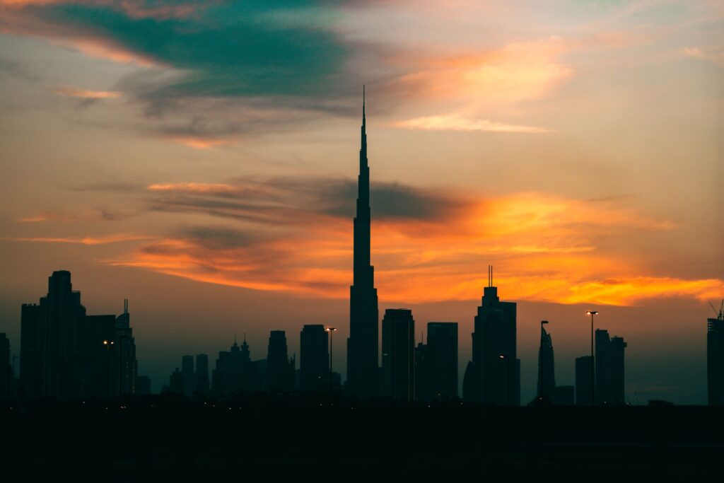 Silhouette of the Dubai skyline against a teal and orange sunset sky
