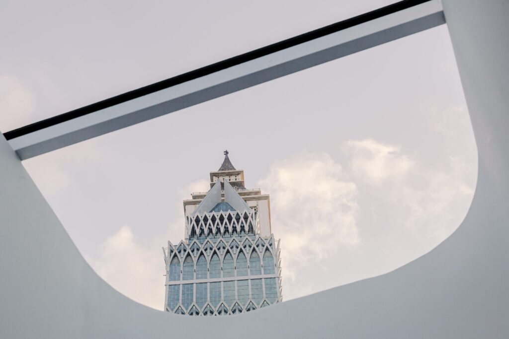 Upward view of a modern high-rise tower with an arched glass facade framed by an architectural overhang, representative of Business Bay's residential tower skyline in Dubai