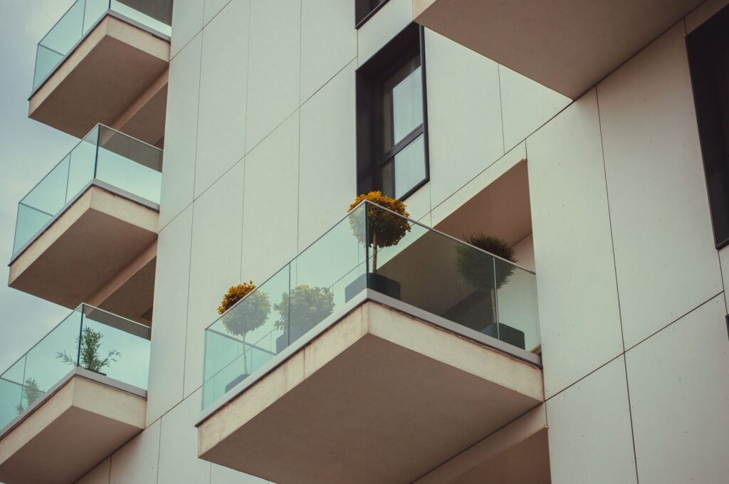 Clean minimalist white apartment balcony facade with glass railings and potted plants, no people, Dubai-plausible architecture