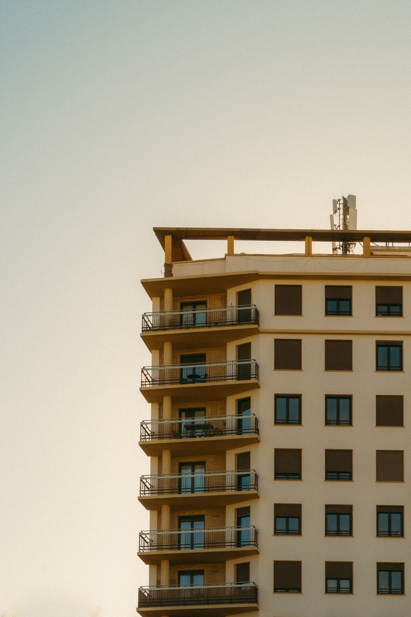 Warm sunset-toned modern apartment building corner with dark balcony railings, representative of Binghatti Sapphires in Dubai Silicon Oasis, Dubai