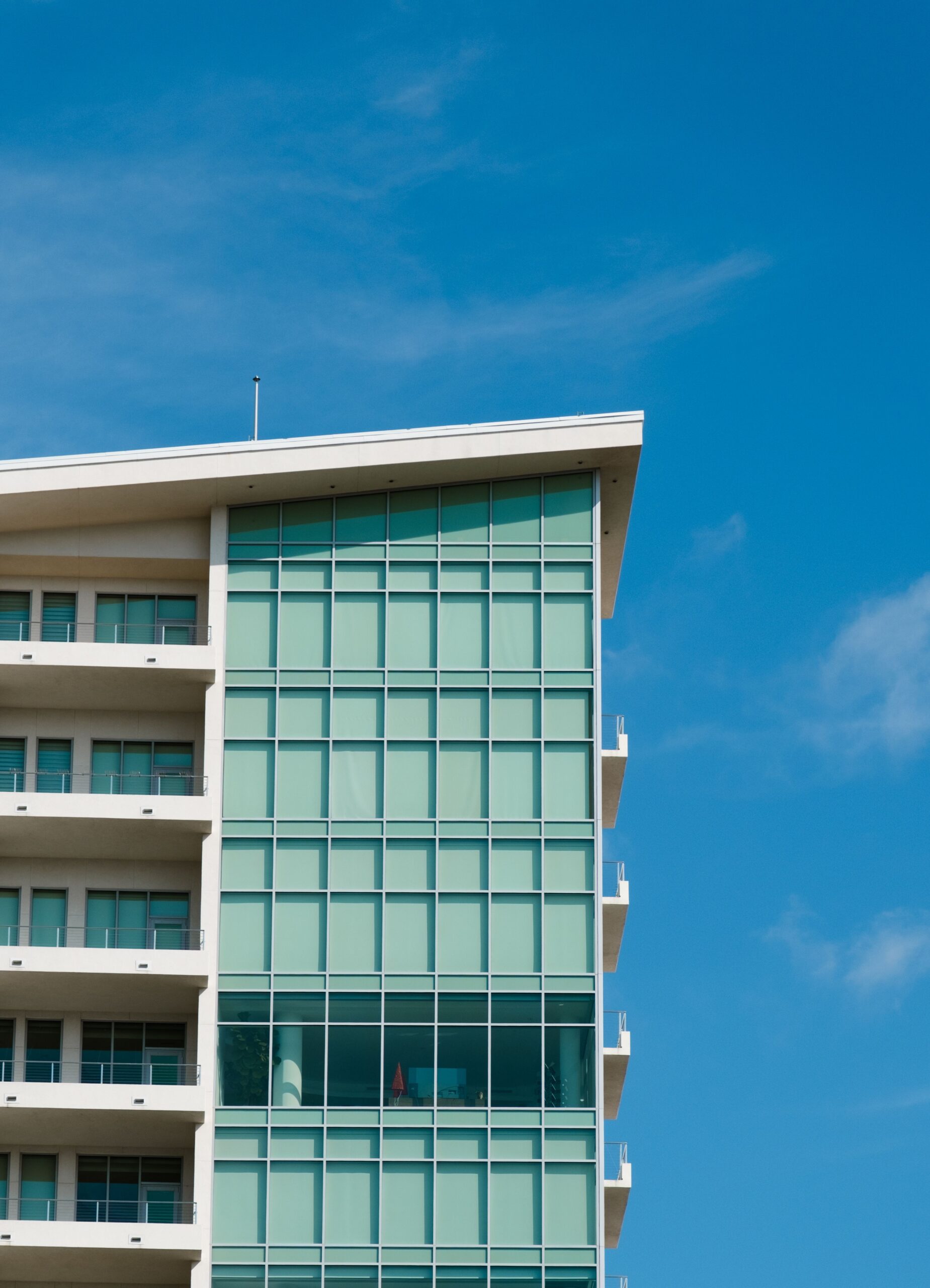 Modern apartment building corner with green-tinted glass and white balconies against a bright blue sky in Dubai