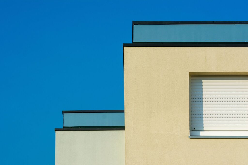 Corner of a modern cream-coloured low-rise apartment building with closed roller shutters against a clear blue sky in Dubai