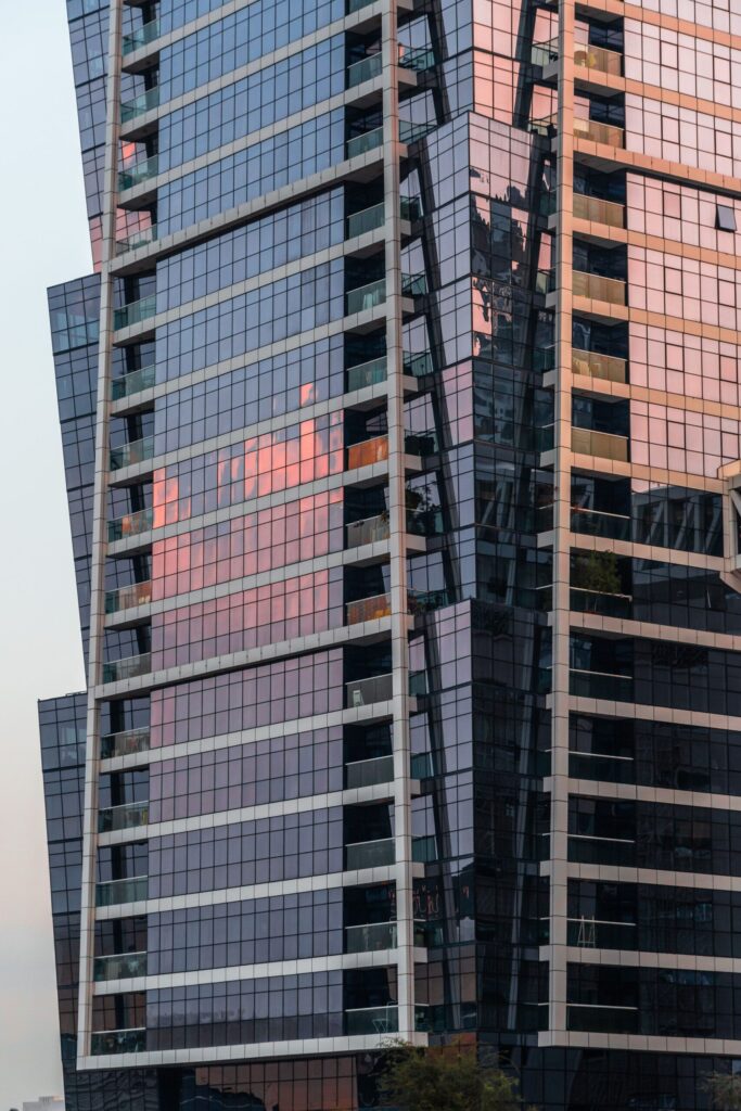 Close-up of an angular glass high-rise tower facade reflecting a sunset sky, Dubai