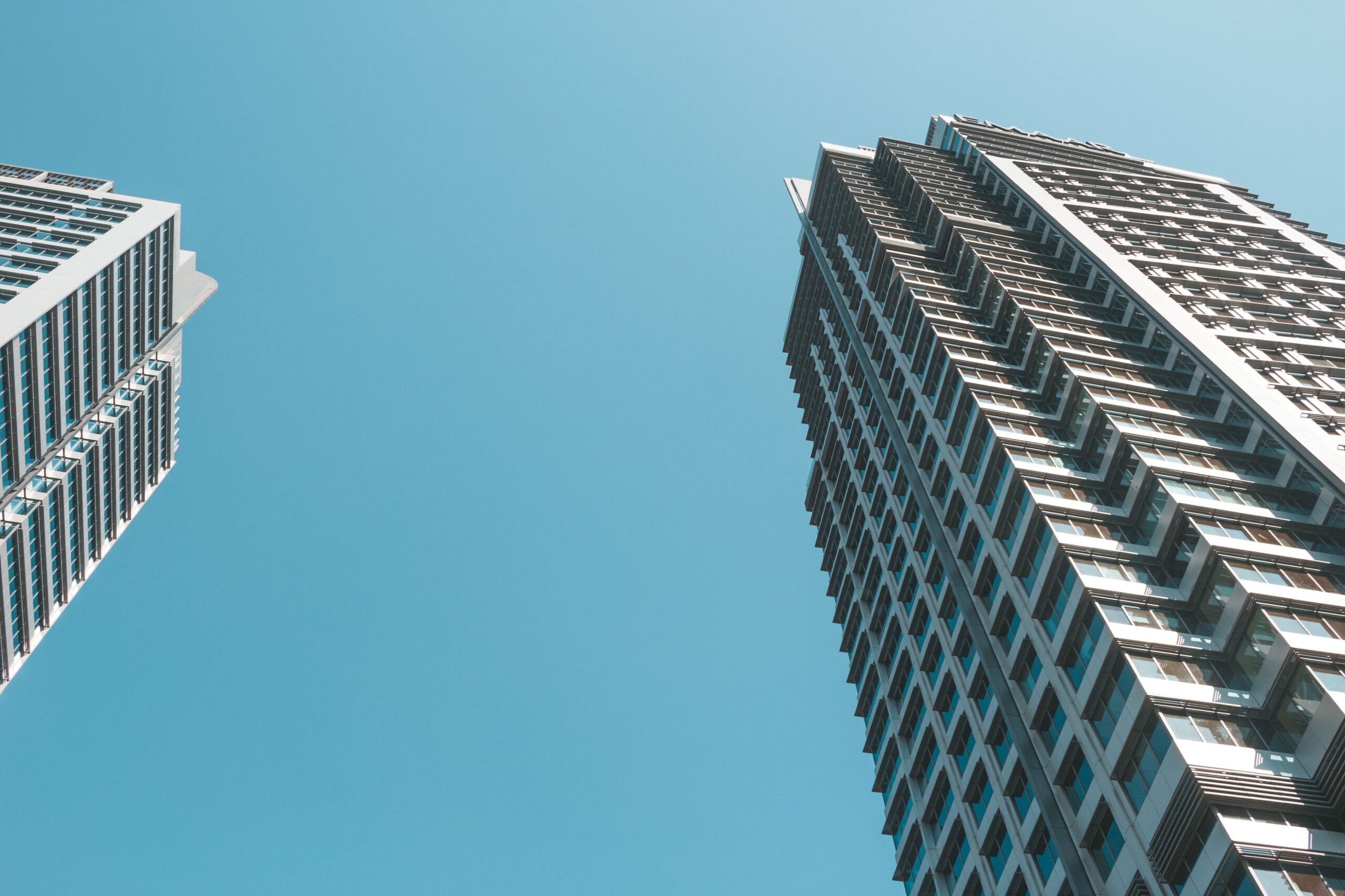 Two modern glass and white high-rise residential towers viewed from a low angle against a clear blue sky, representative of Azizi Feirouz in Al Furjan, Dubai