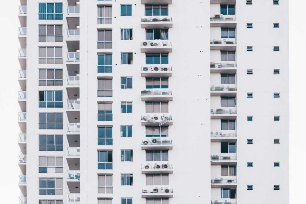 Clean white multi-storey apartment facade with glass balconies and AC condenser units, representative of Oasis High Park in Dubai Silicon Oasis, Dubai