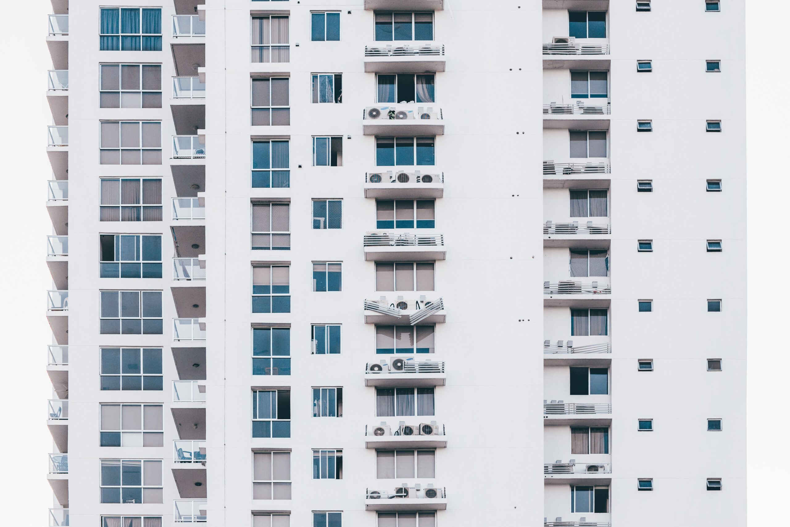 Clean white multi-storey apartment facade with glass balconies and AC condenser units, representative of Oasis High Park in Dubai Silicon Oasis, Dubai