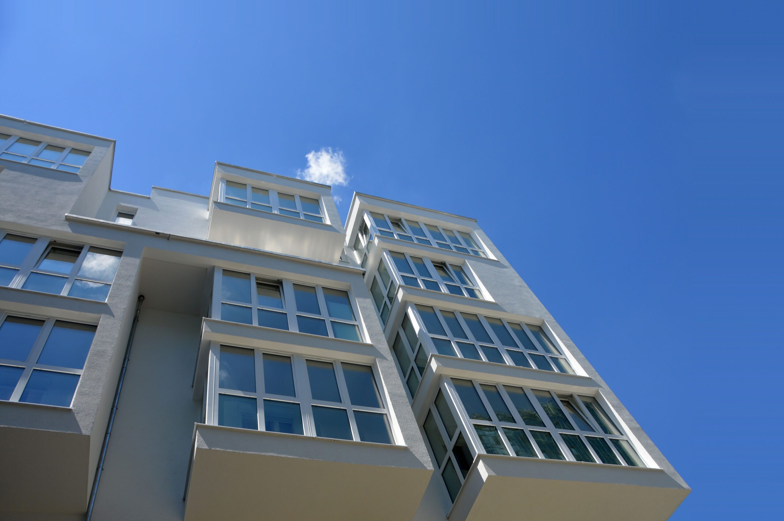 Low-angle view of a clean white modern low-rise apartment building against a clear blue sky, representative of Al Durar Tower B in DubaiLand Residence Complex, Dubai