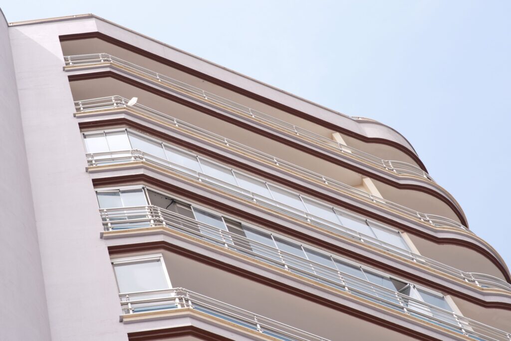 Low angle view of a modern cream-toned apartment building with a curved corner and dark red-trimmed balconies against a clear sky in Dubai
