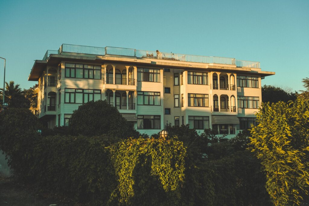 Cream-toned low-rise apartment building with arched balconies surrounded by greenery at sunset, Dubai