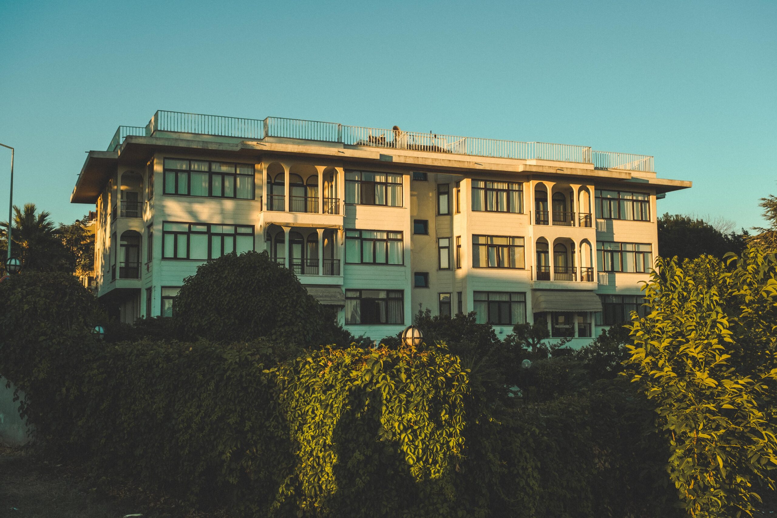 Cream-toned low-rise apartment building with arched balconies surrounded by greenery at sunset, Dubai