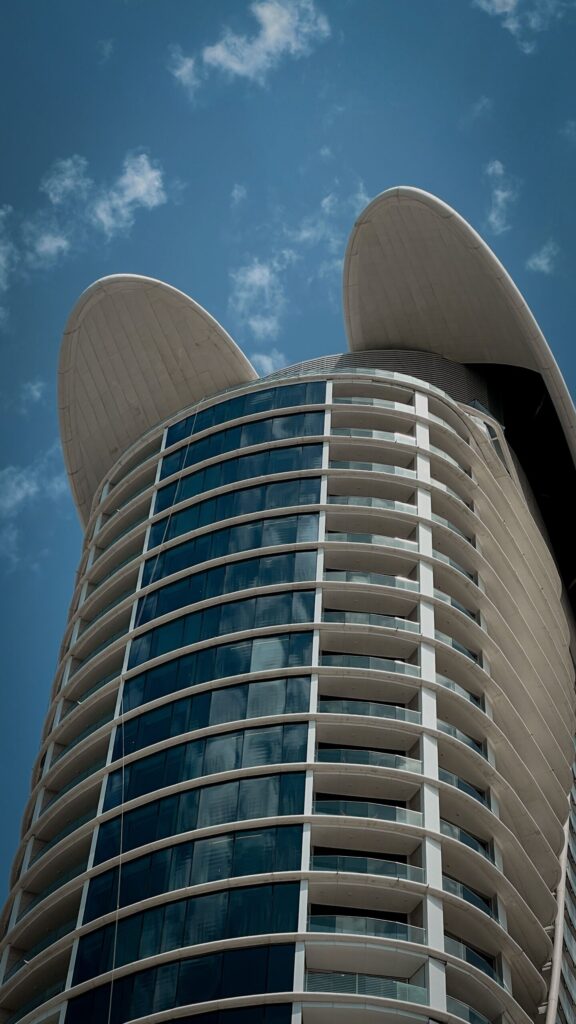 Modern curved-top residential tower with balconies against a clear blue sky in Dubai