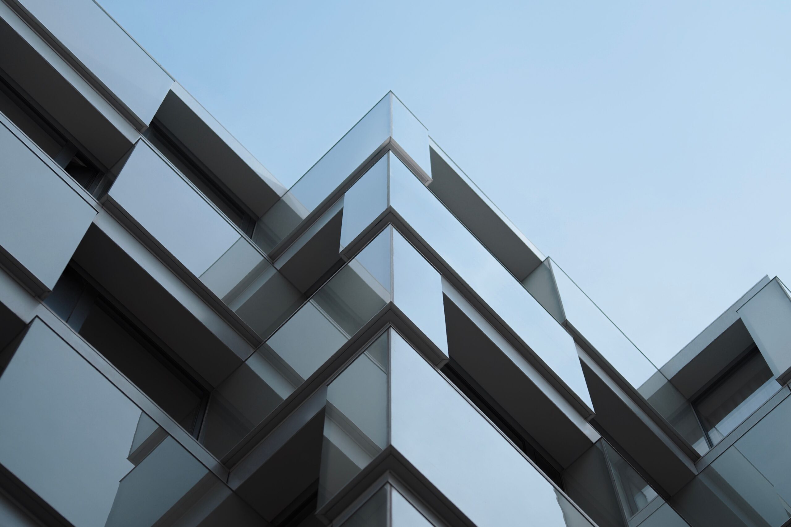 Low angle view of a modern glass apartment building corner with a symmetrical zigzag balcony pattern against a clear blue sky in Dubai