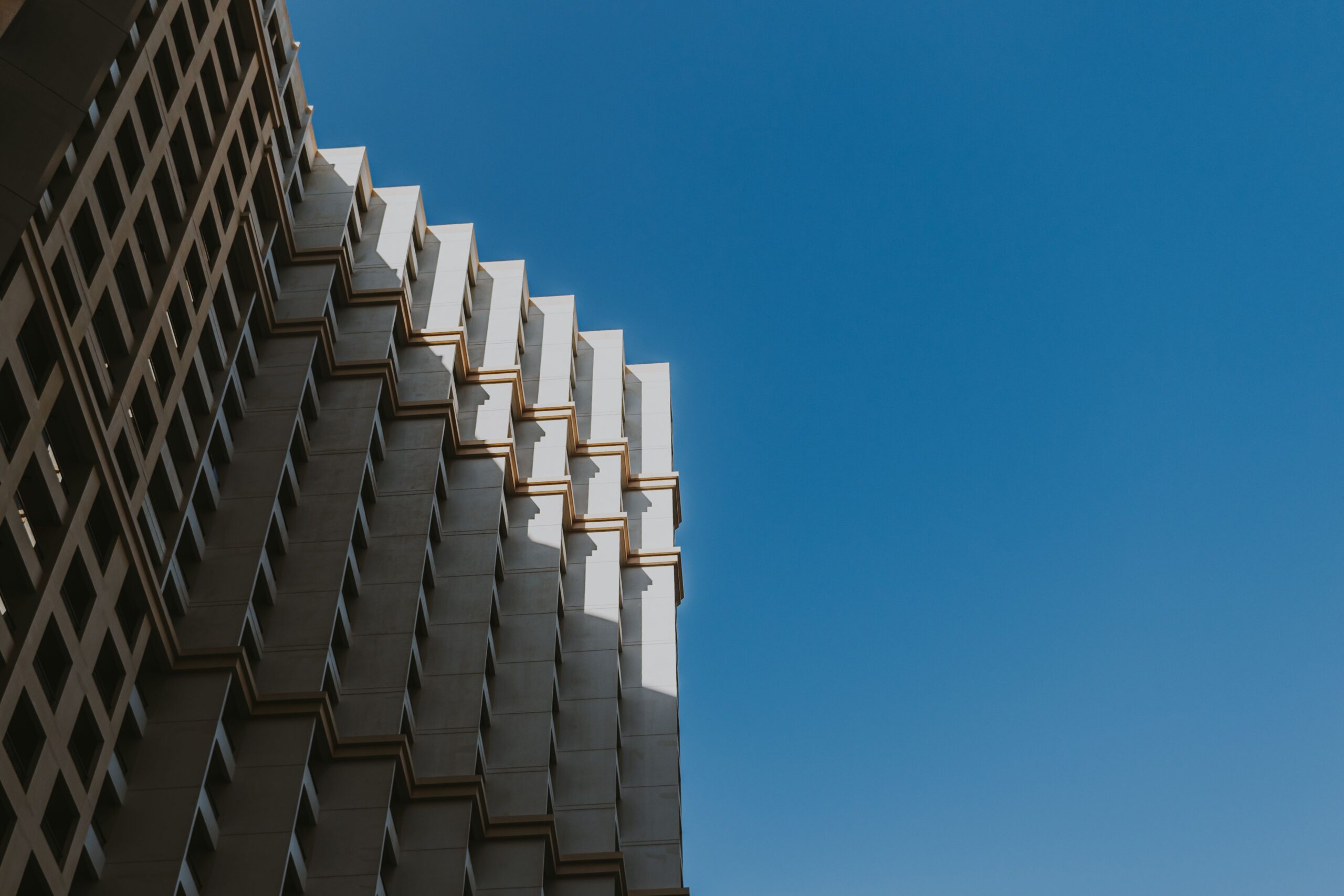 High-rise building corner with a repeating angled balcony pattern against a bright blue sky in Dubai