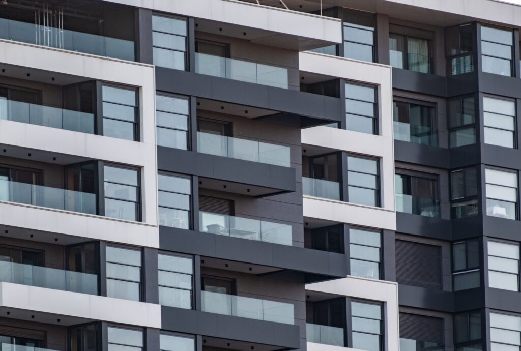 Modern grey and white apartment building facade with dark glass balconies, similar in style to Edmonton Elm, JVT