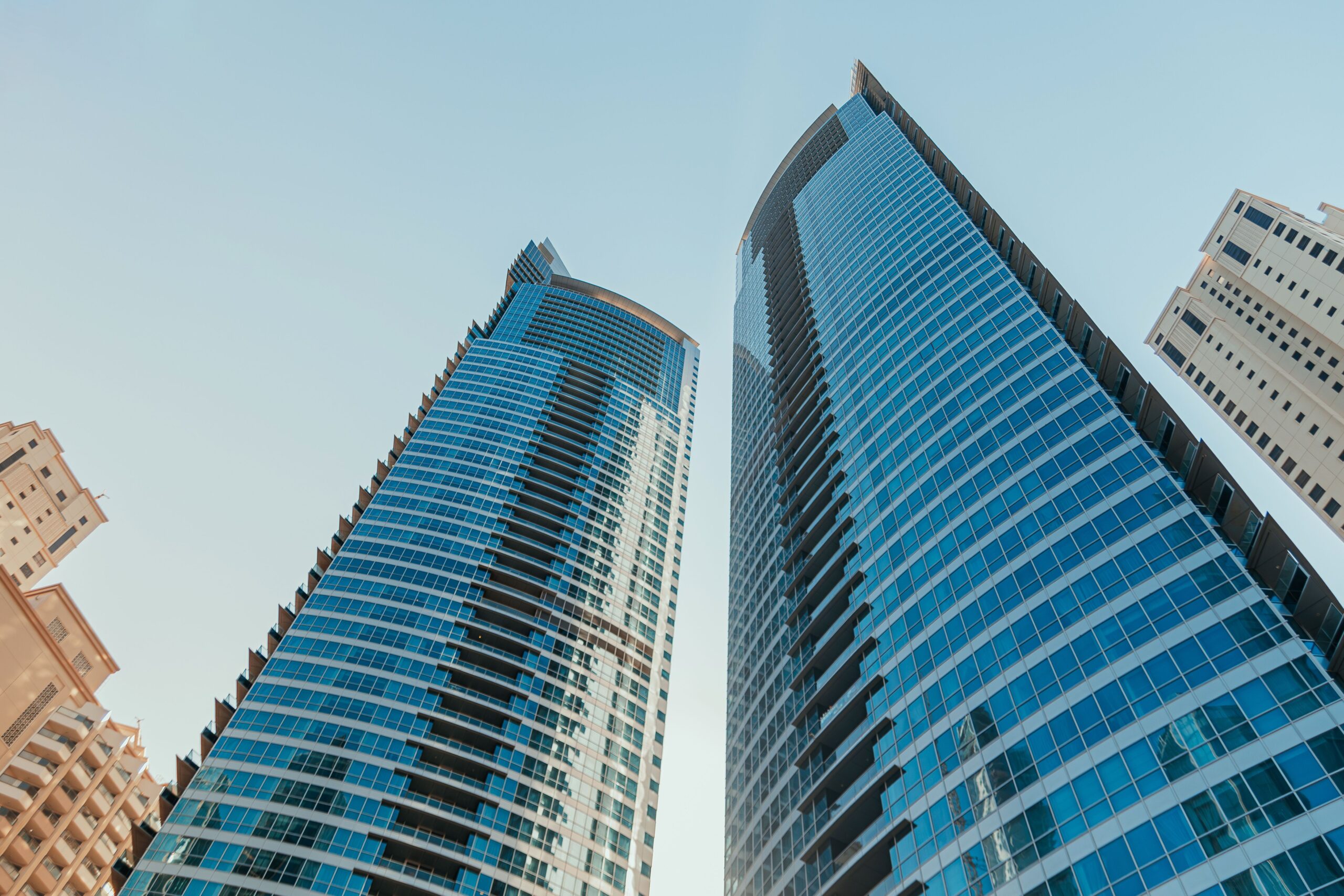 Low-angle view of two modern glass residential towers in Dubai Marina against a clear blue sky