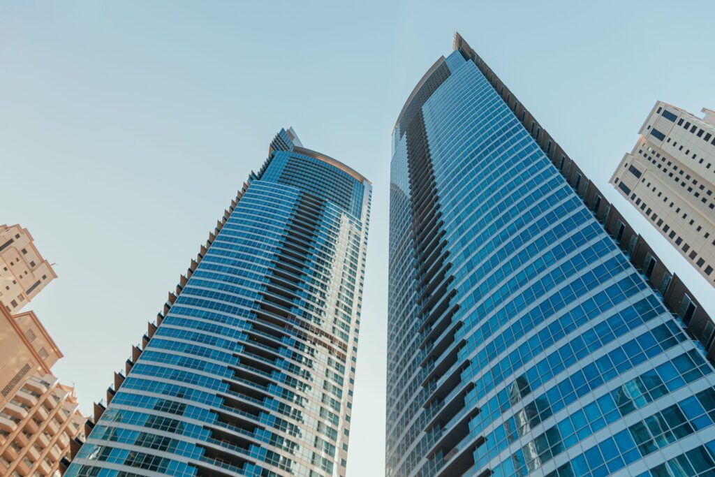 Upward angle on two adjacent Dubai Marina glass towers against a pale blue sky near Ariyana Tower