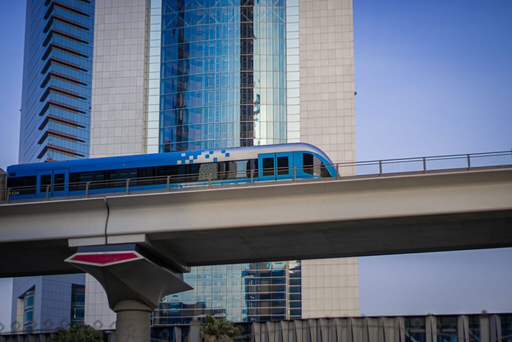 Blue metro train crossing a viaduct above a Dubai cityscape