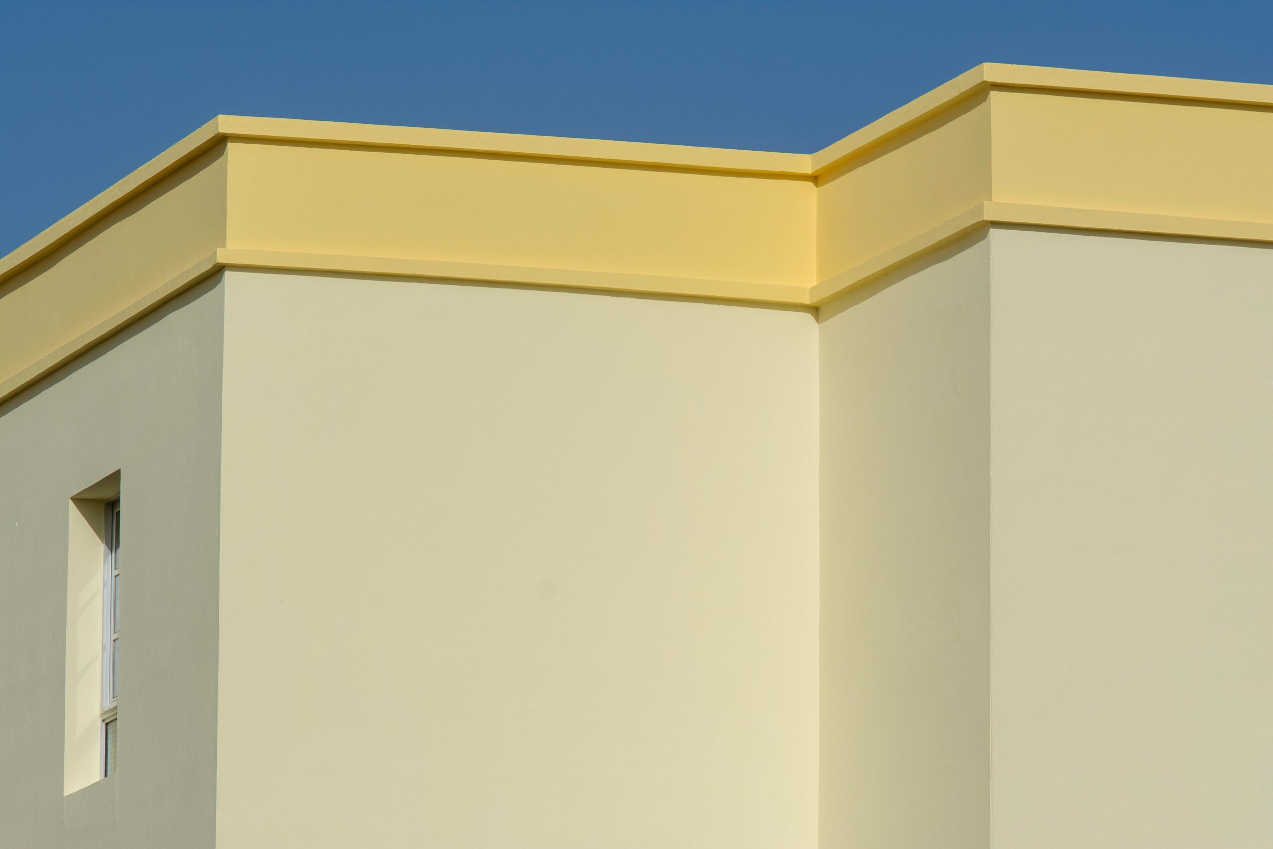Minimalist cream and yellow apartment building corner with a single window against a clear blue sky in Dubai