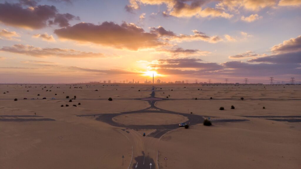 Desert road roundabout at sunset with the Dubai skyline on the horizon