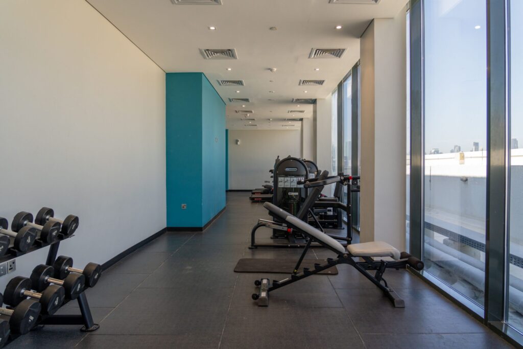 Modern indoor gym with a Dubai skyline view through floor-to-ceiling windows, echoing Parkside Views' own fully-equipped gym amenity in Dubai Hills Estate