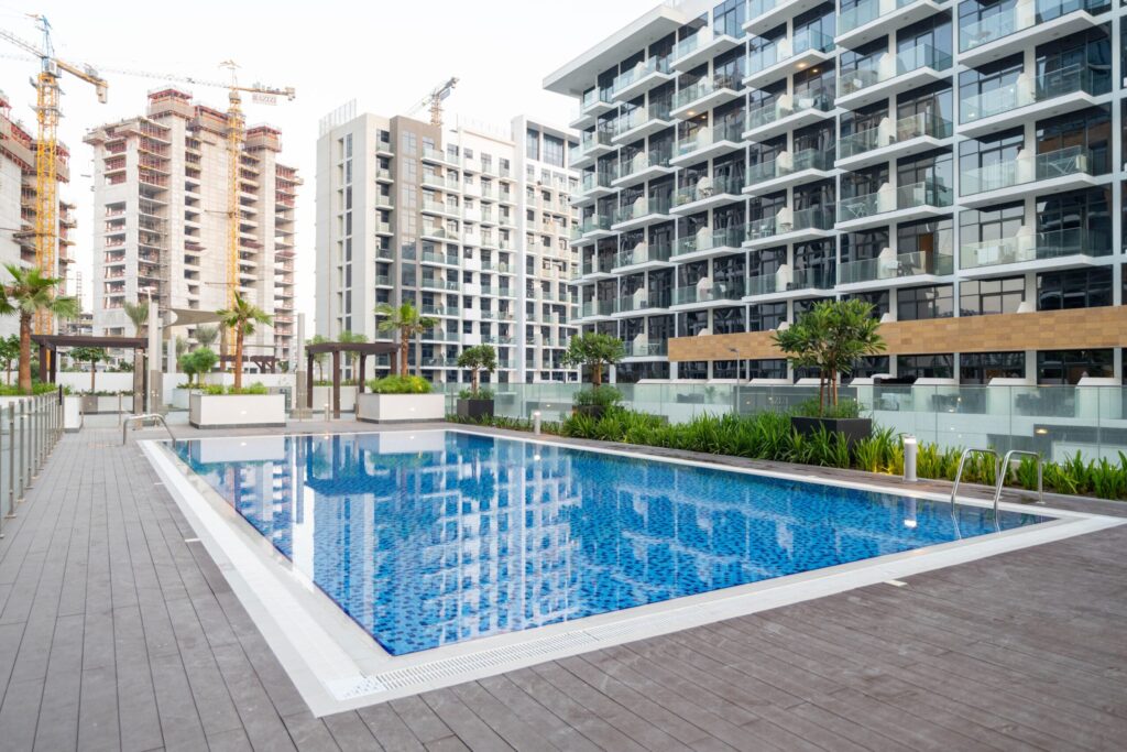 Landscaped swimming pool deck in front of mid-rise residential buildings near Plazzo Heights, JVC