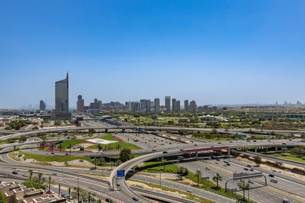 Aerial daytime view of a Dubai highway interchange with a flag-striped spire tower against a clear blue sky