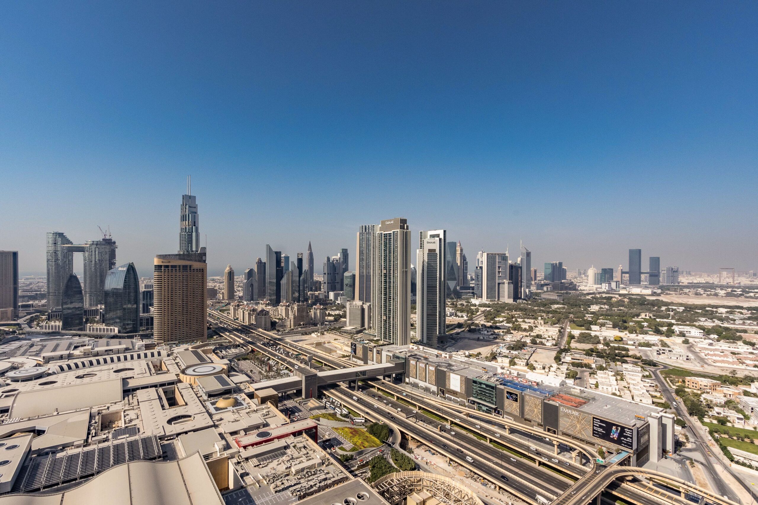 Panoramic aerial view of Downtown Dubai's skyline with modern high-rise towers and Sheikh Zayed Road under a clear blue sky
