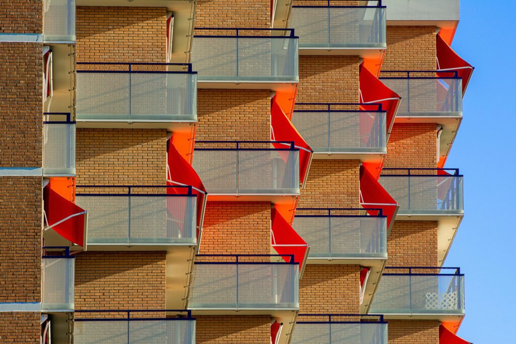 Modern apartment building exterior with orange geometric zigzag balconies and glass railings under a clear blue sky, Dubai, representative of Lincoln Park B, Arjan