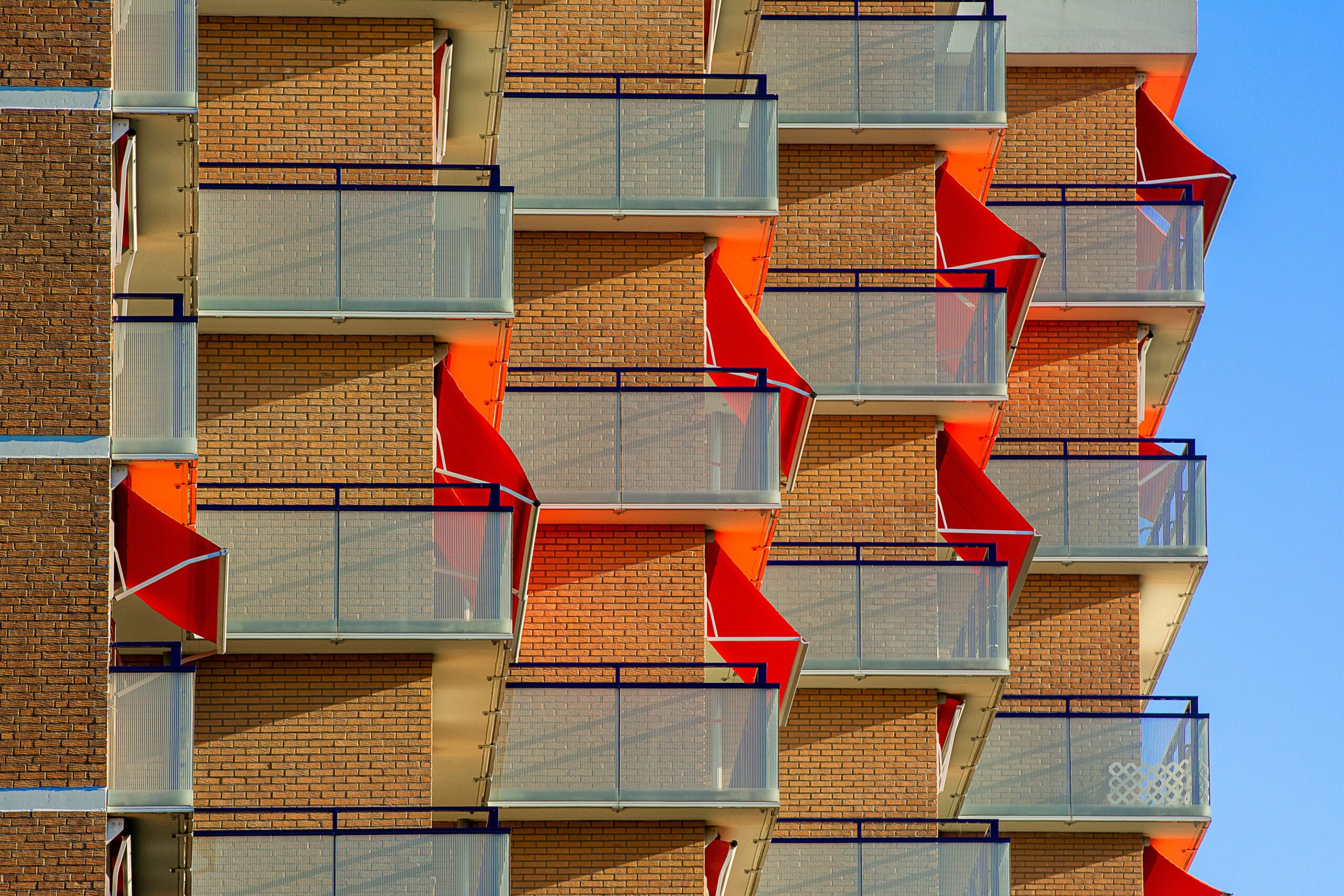 Modern apartment building exterior with orange geometric zigzag balconies and glass railings under a clear blue sky, Dubai, representative of Lincoln Park B, Arjan