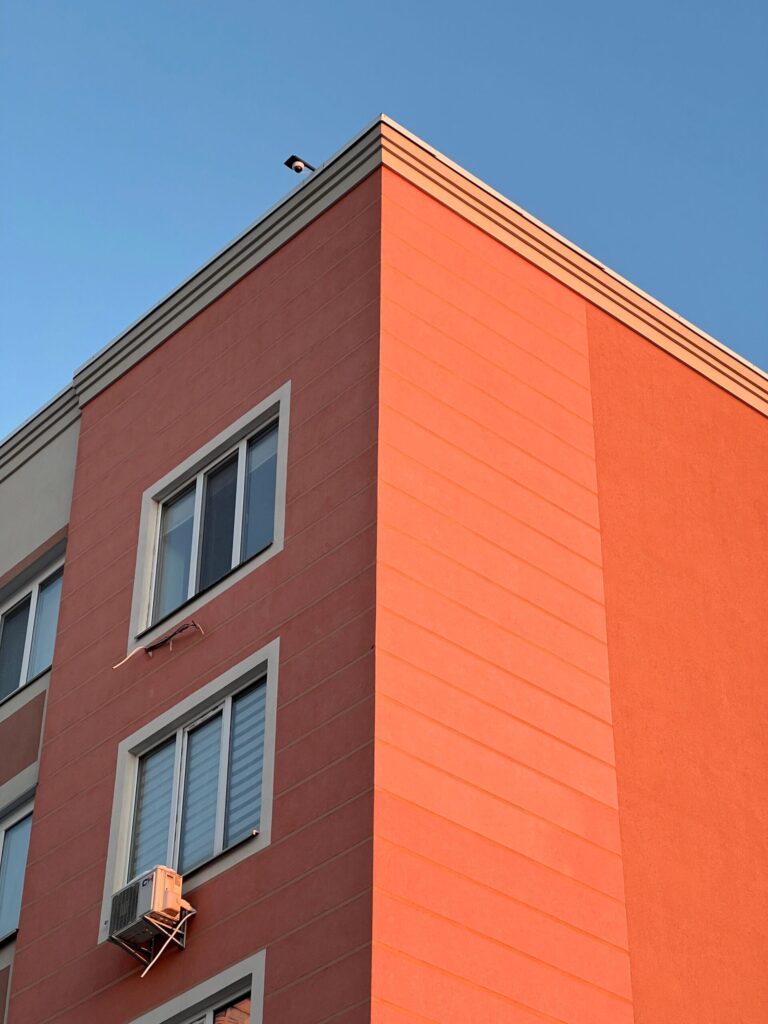 Corner of a modern orange and terracotta low-rise apartment building with white-framed windows against a clear blue sky in Dubai