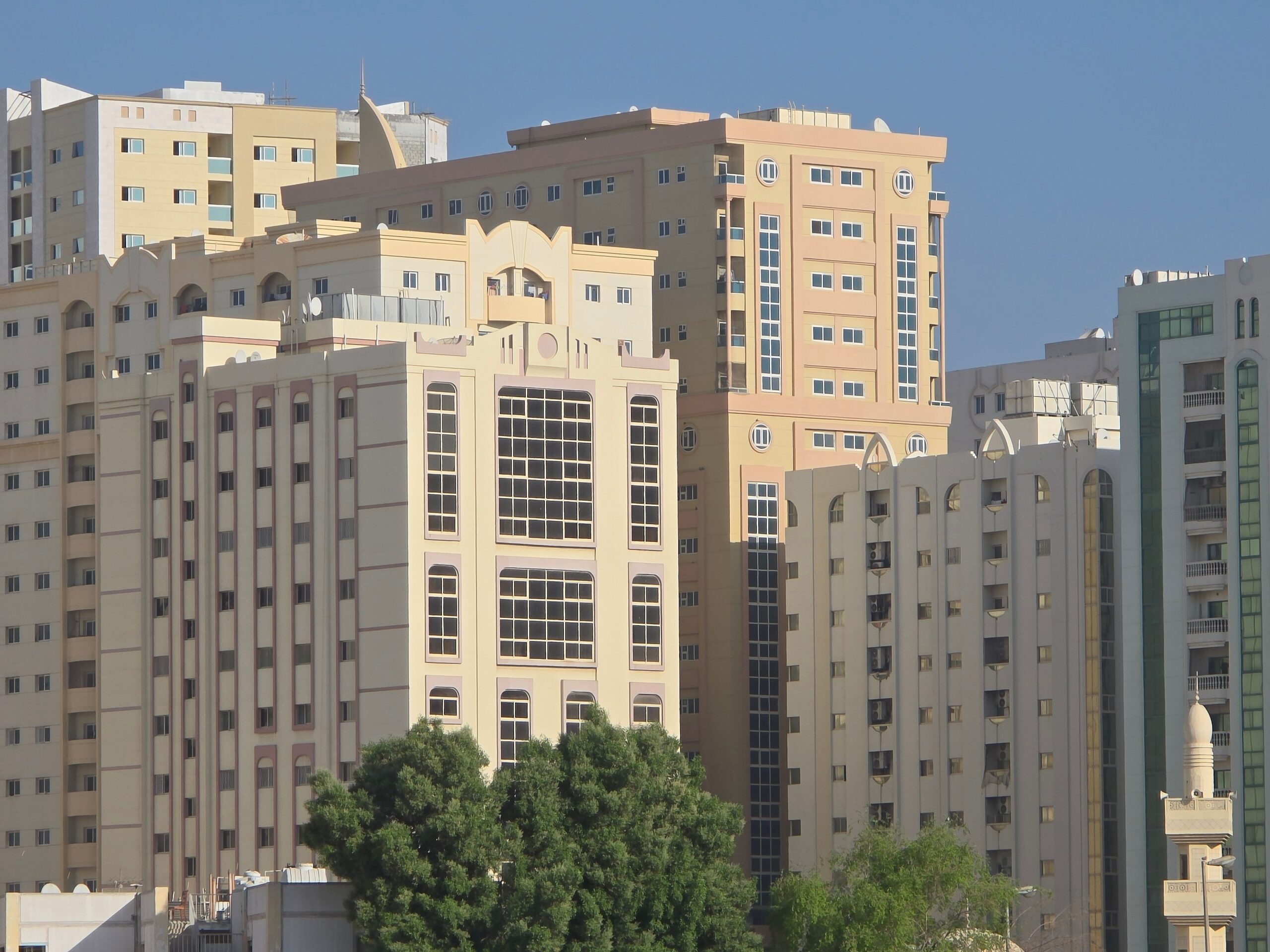 Cluster of mid-rise Dubai apartment buildings with decorative Arabian-influenced facades under a clear blue sky, representative of Ajmal Sarah Tower in DubaiLand Residence Complex, Dubai