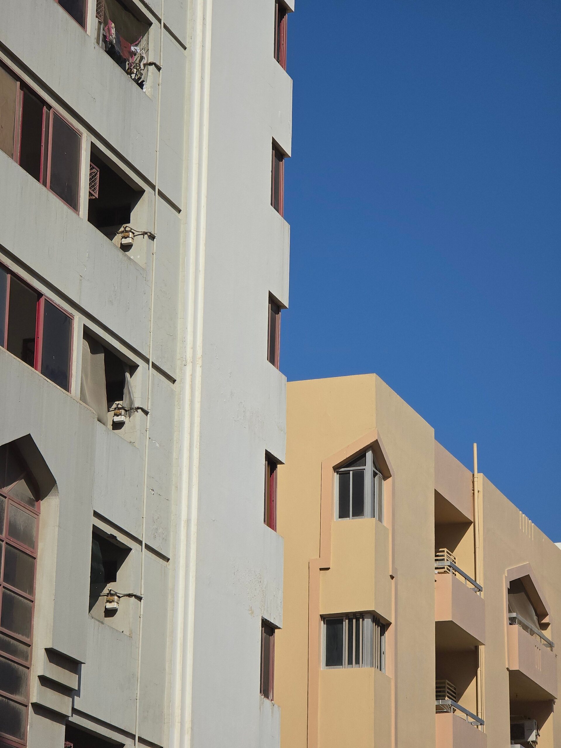 Angled view of mid-rise white and pastel-peach Dubai apartment buildings with arched window details under a clear blue sky, representative of Al Durar Tower A in DubaiLand Residence Complex, Dubai