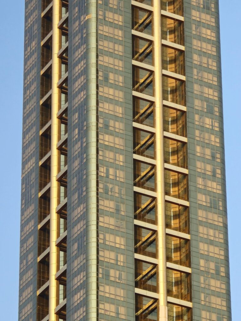 Close-up of a modern high-rise tower corner with gold diagonal facade bracing against a pale blue sky in Dubai