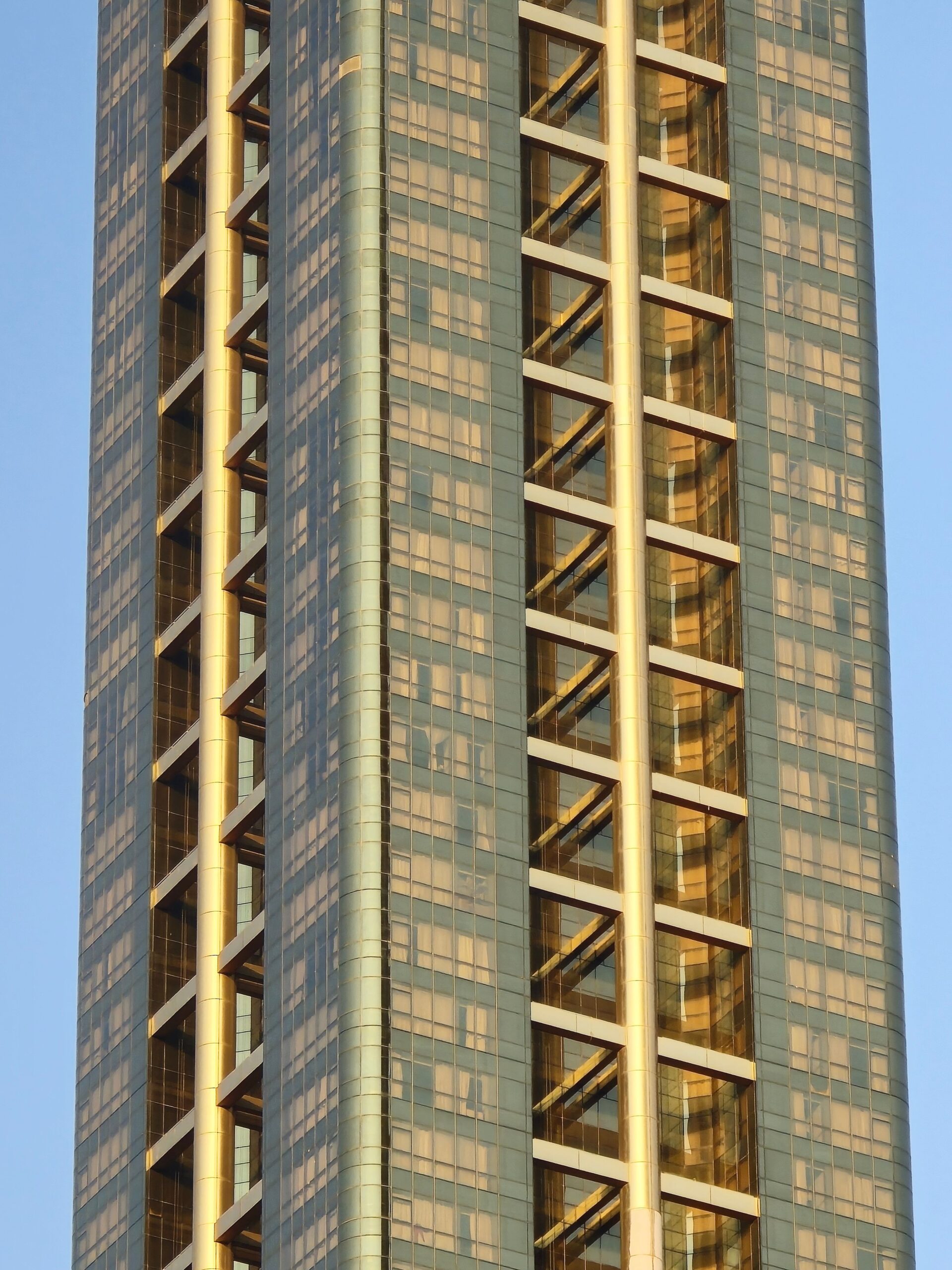 Close-up of a modern high-rise tower corner with gold diagonal facade bracing against a pale blue sky in Dubai