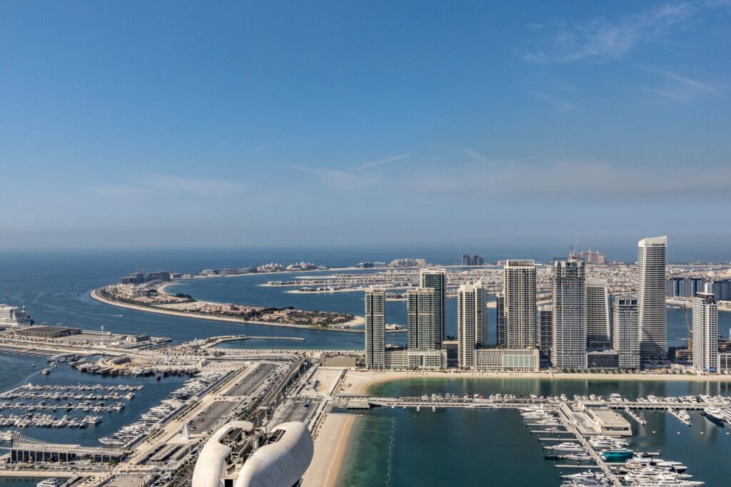 Aerial view of Dubai Marina skyline with the Palm Jumeirah crescent visible in the background under a clear blue sky